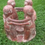 Vier rotbraune stehende Tonfiguren mit verbundenen Armen auf einer Wiese